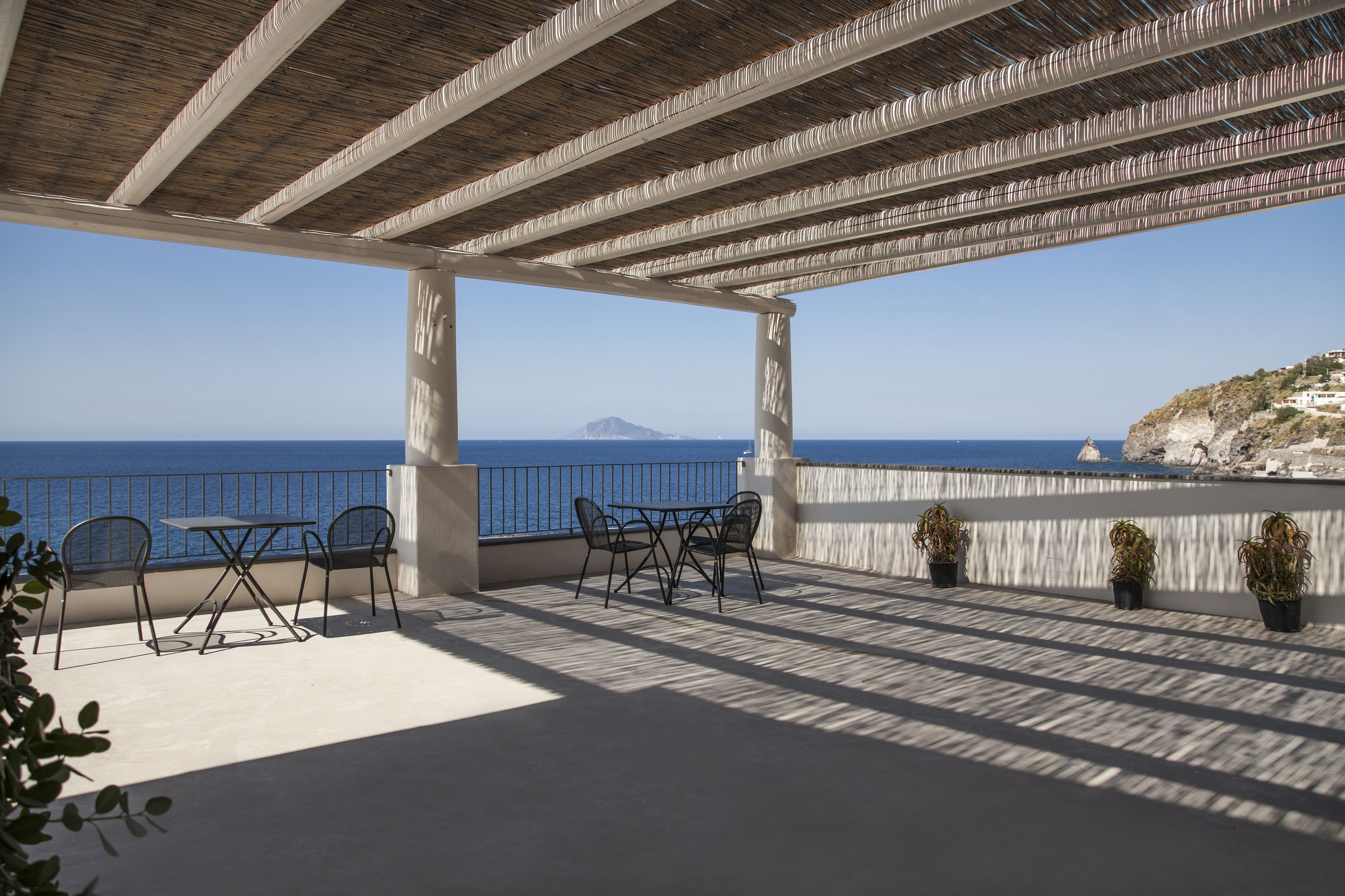 Un espace extérieur abrité, aménagé avec des sièges, offrant une vue sur la mer et sur une montagne lointaine.