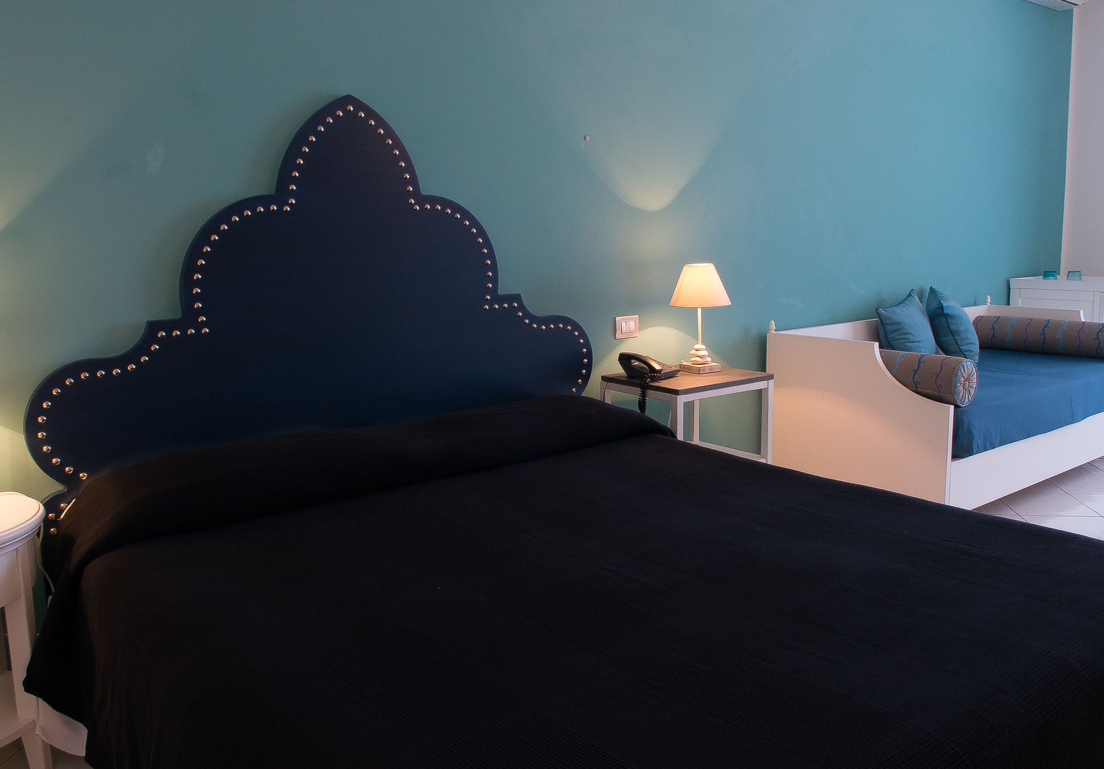 A bedroom with a dark blue headboard, a bedside table with a lamp, a phone, and a bed with blue bedding.