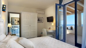 A hotel room with a bed, a desk, a TV, a wardrobe, and a balcony with a view of the sea. - Hotel Cutimare (Lipari)