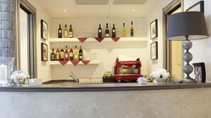 A reception area with a counter displaying various bottles and glasses, a red vintage espresso machine, and a wall with repeated text. - Hotel Cutimare (Lipari)