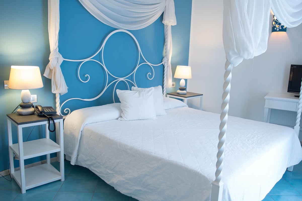 A bedroom with a four-poster bed, white bedding, two bedside tables with lamps, and a television on a stand.