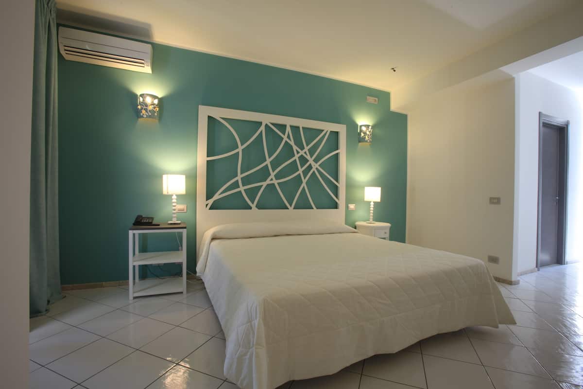 A bedroom with a large bed, a nightstand, a wall-mounted air conditioner, and two wall sconces.