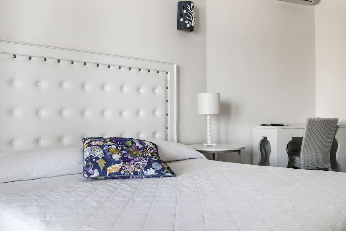 A neatly made bed with a floral pillow, a bedside table with a lamp, and a chair.