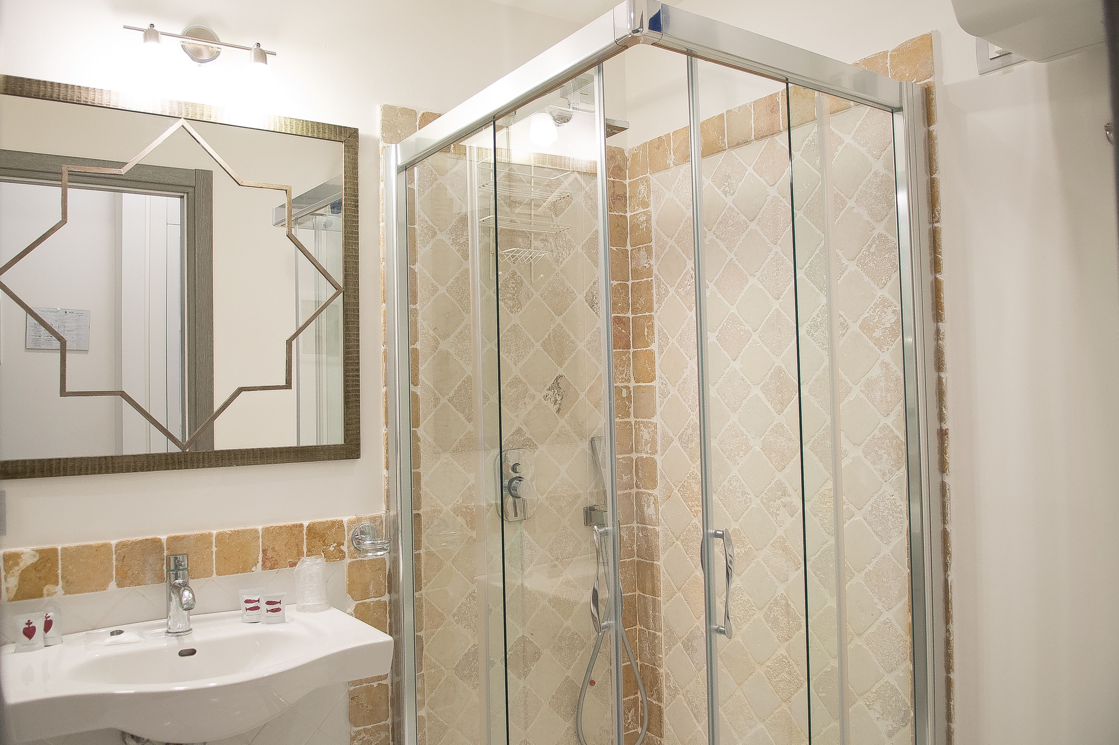 Une salle de bain avec une douche à parois de verre, un lavabo avec un miroir au-dessus et un mur recouvert de carreaux.