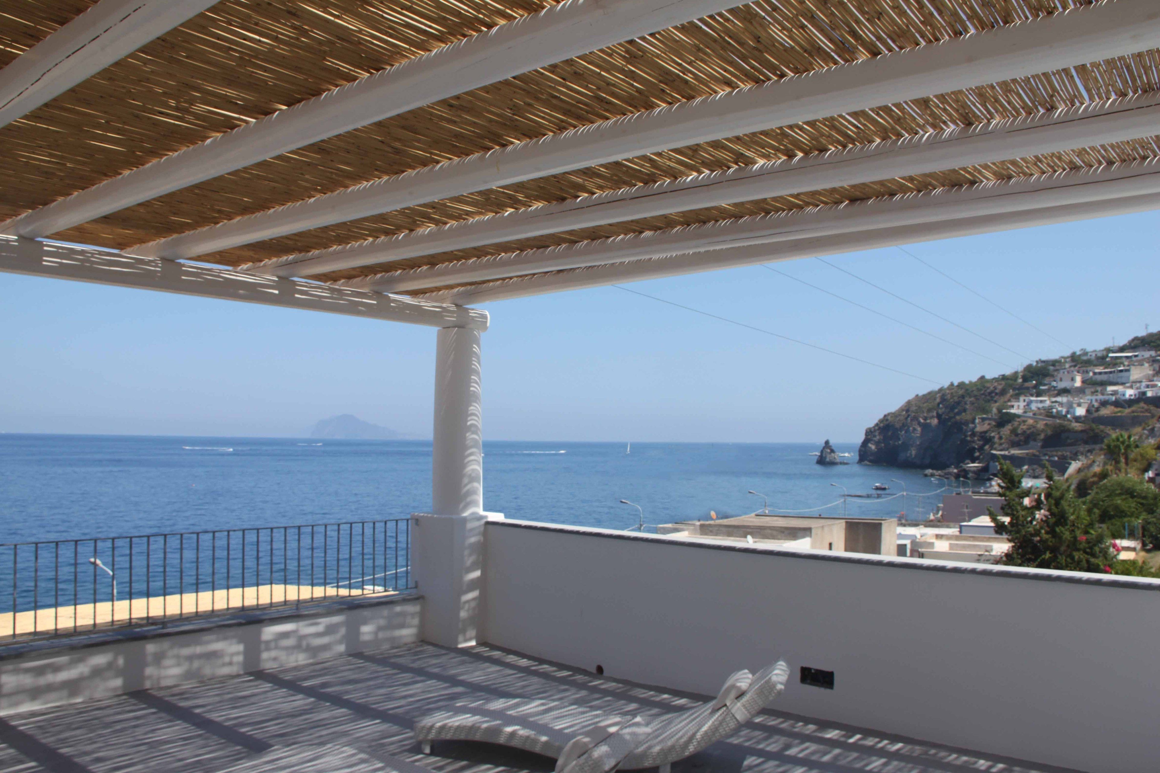 Un balcon donnant sur la mer, une chaise et un toit de chaume.