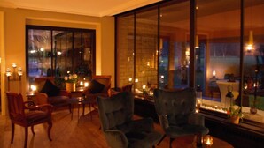A cozy room with a large window, comfortable seating, and a stone fireplace. - Hotel de la Gaichel (Habscht)