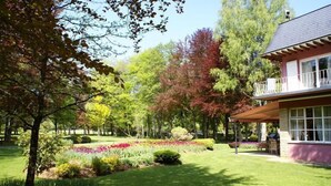 A well-maintained garden with a variety of plants and a lawn, a house with a balcony, and a clear sky. - Hotel de la Gaichel (Habscht)