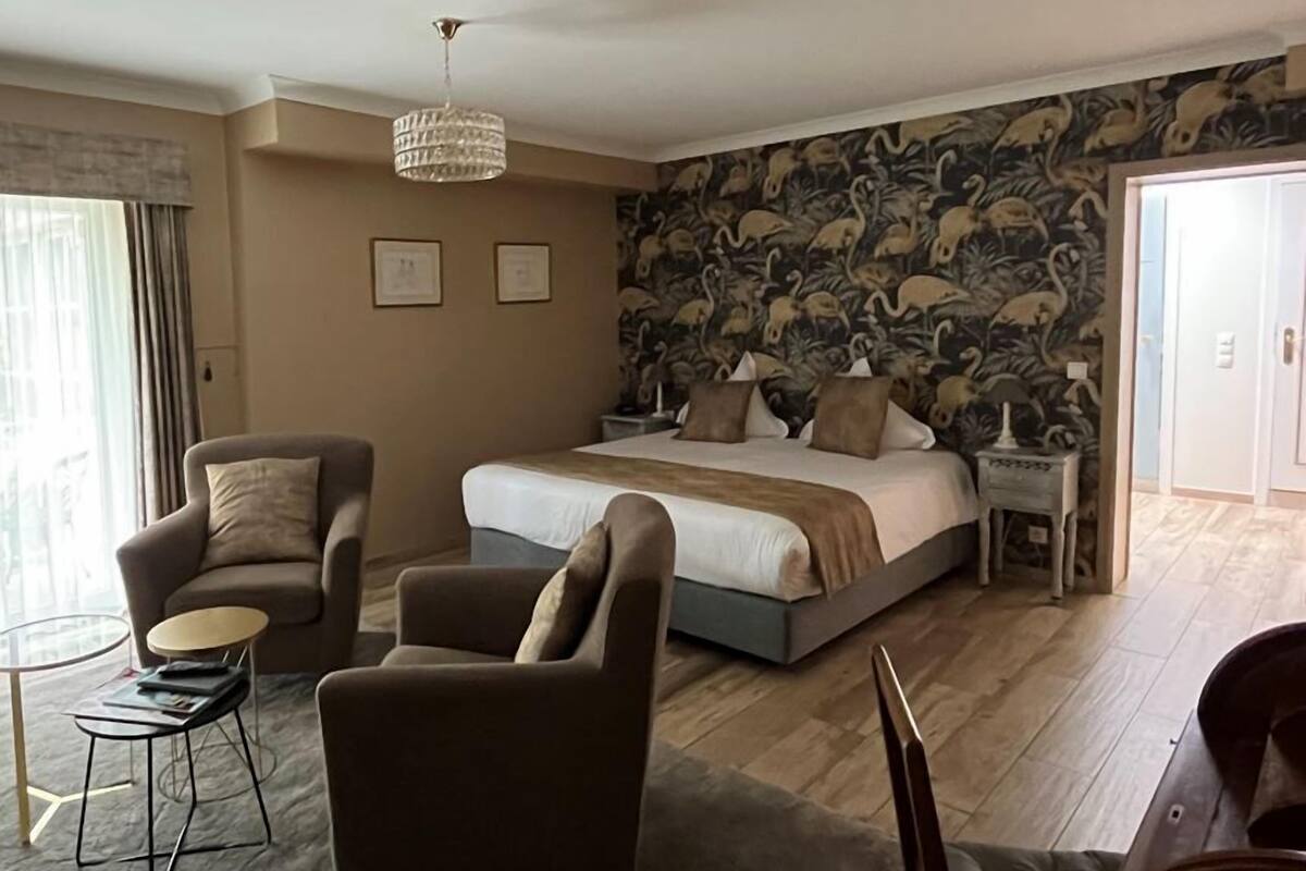 Ein Schlafzimmer mit einem großen Bett, zwei Sessel, einem kleinen Tisch und einer Deckenleuchte.