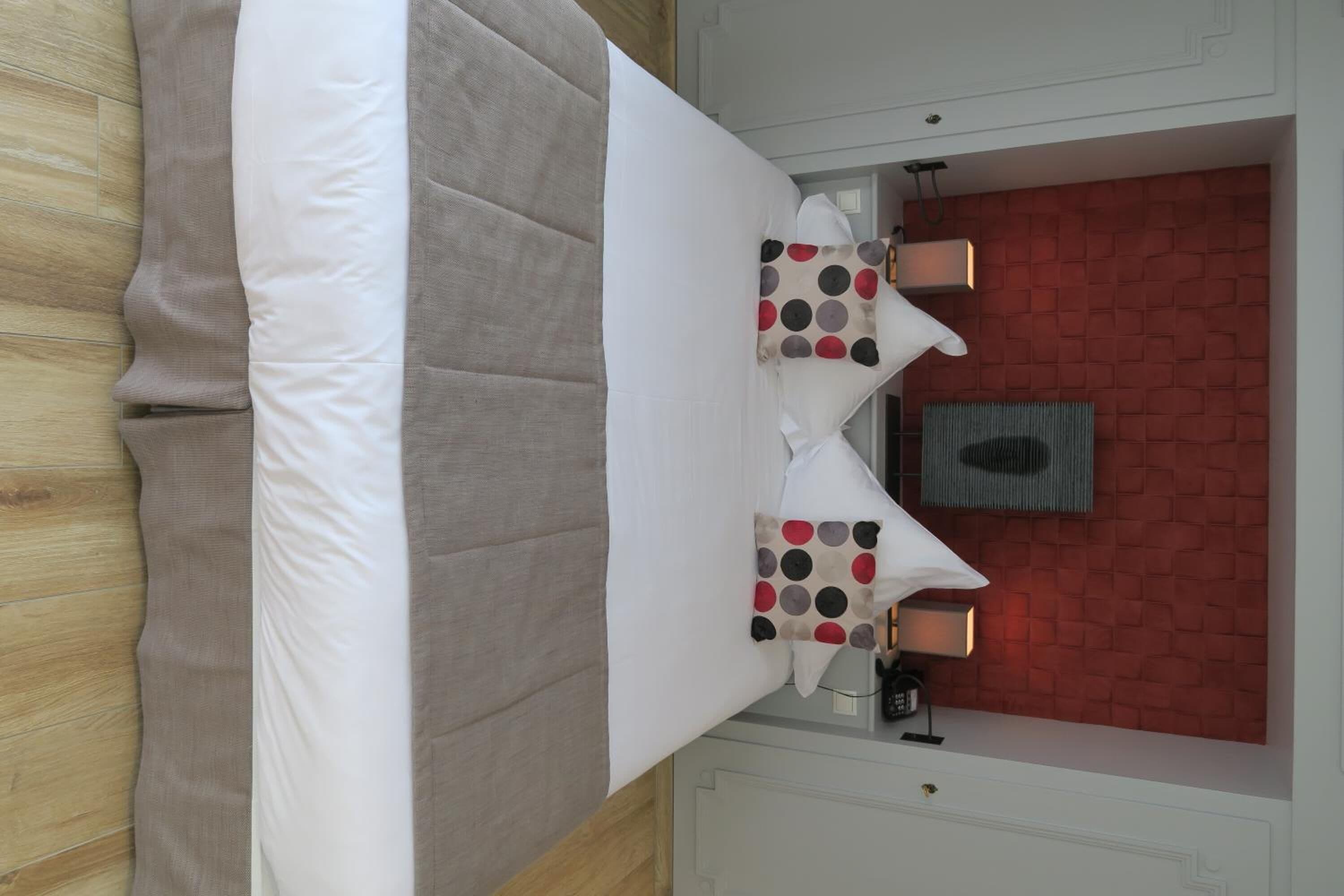 Een hotelkamer met een bed, twee kussens met stipjes, een nachtkastje, een lamp en een rode bakstenen muur.