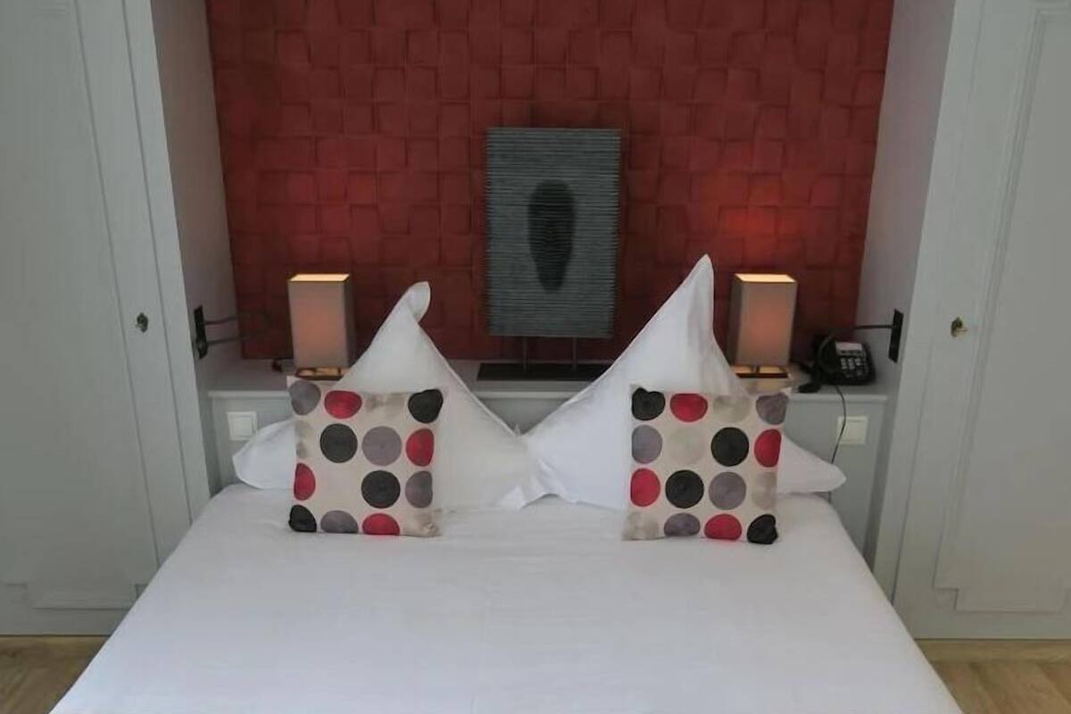Ein ordentlich bezogenes Bett mit grauer Tagesdecke und zwei Kissen mit Punkten.