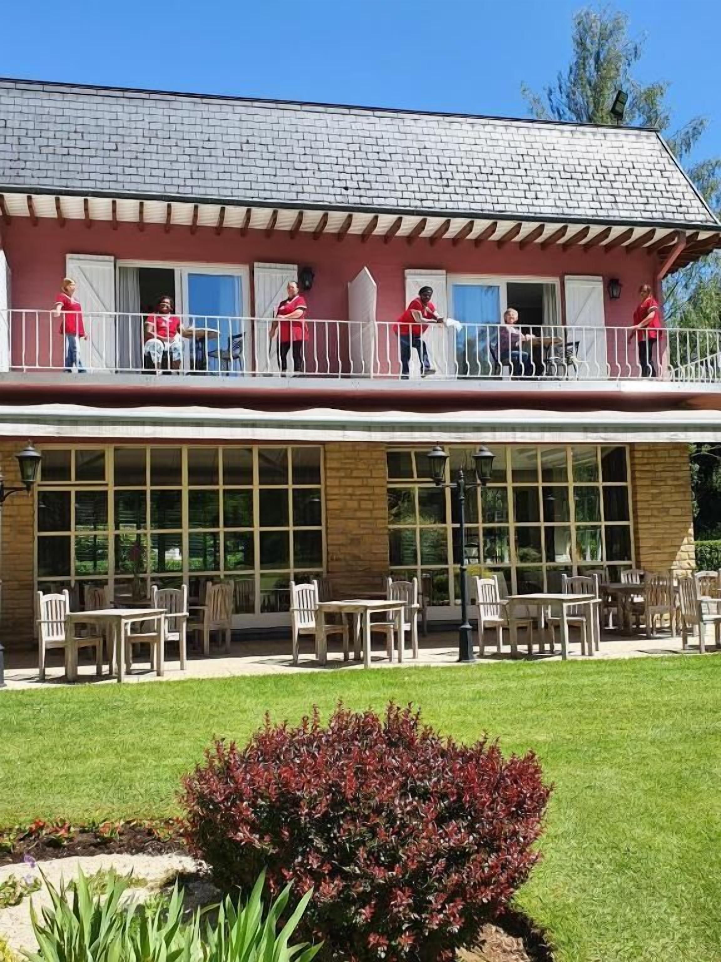 Ein Gebäude mit einem Balkon, Sitzgelegenheiten im Freien und einem gepflegten Rasen.