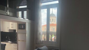 A modern living room with a sectional sofa, a kitchen area, and a large window with a view of a building with a dome. - Hostal Abadía Madrid (Madrid)