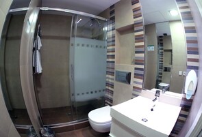 A modern bathroom with a glass-enclosed shower, a white toilet, and a sink with a mirror.