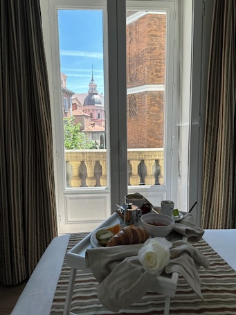 A hotel room with a balcony, a breakfast tray with croissants, coffee, and fruit, and a bed with striped bedding.