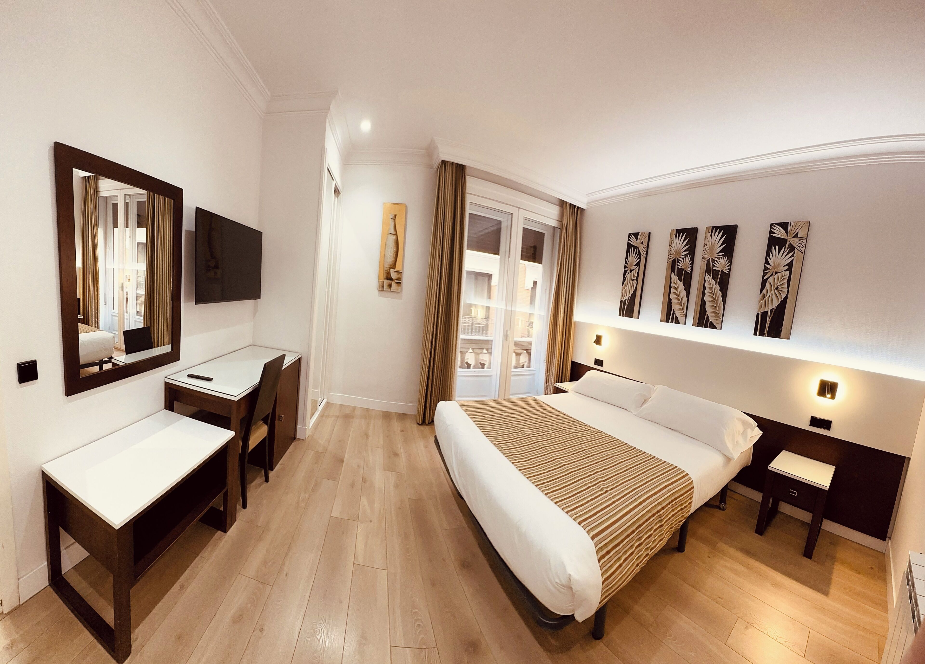 A hotel room with a bed, a desk, a chair, a TV, and a window with curtains.