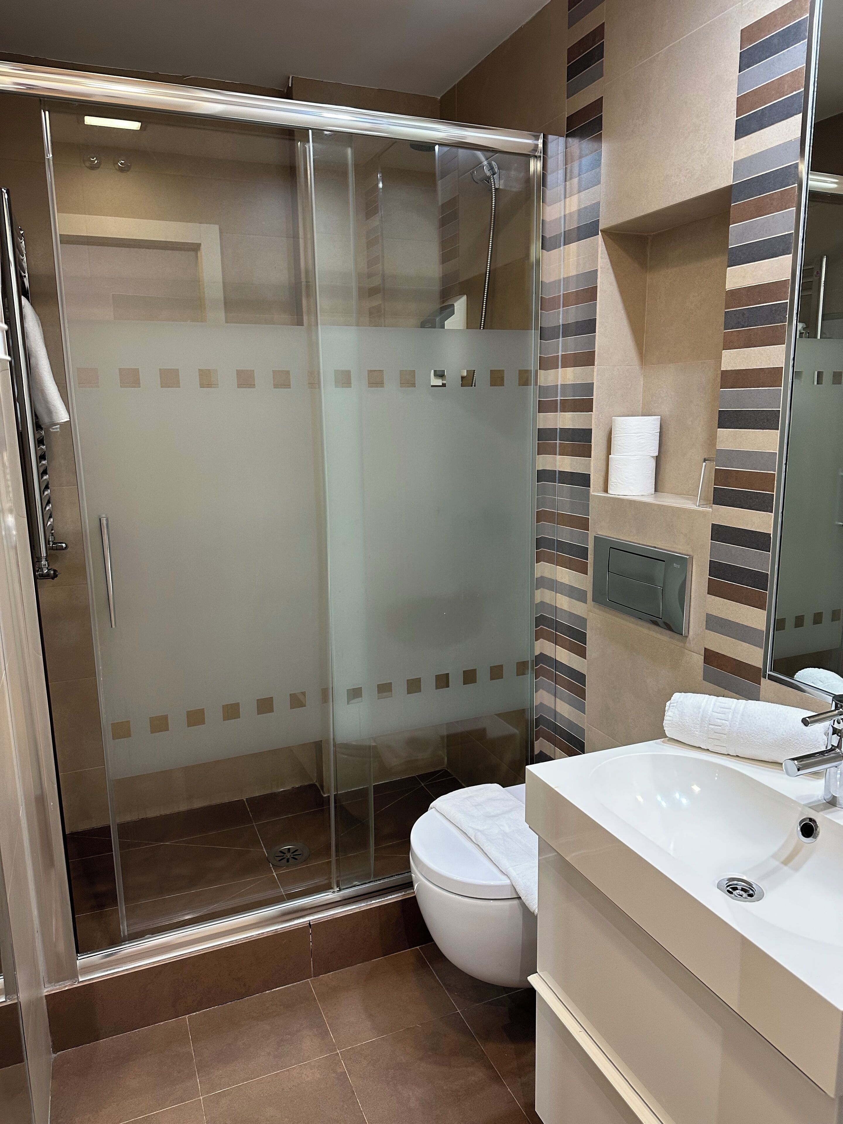 Un baño moderno con ducha envuelta en vidrio, inodoro y lavamanos con espejo.