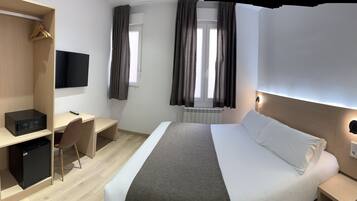 Una habitación de hotel con una cama, un escritorio con una computadora, un armario y un televisor.