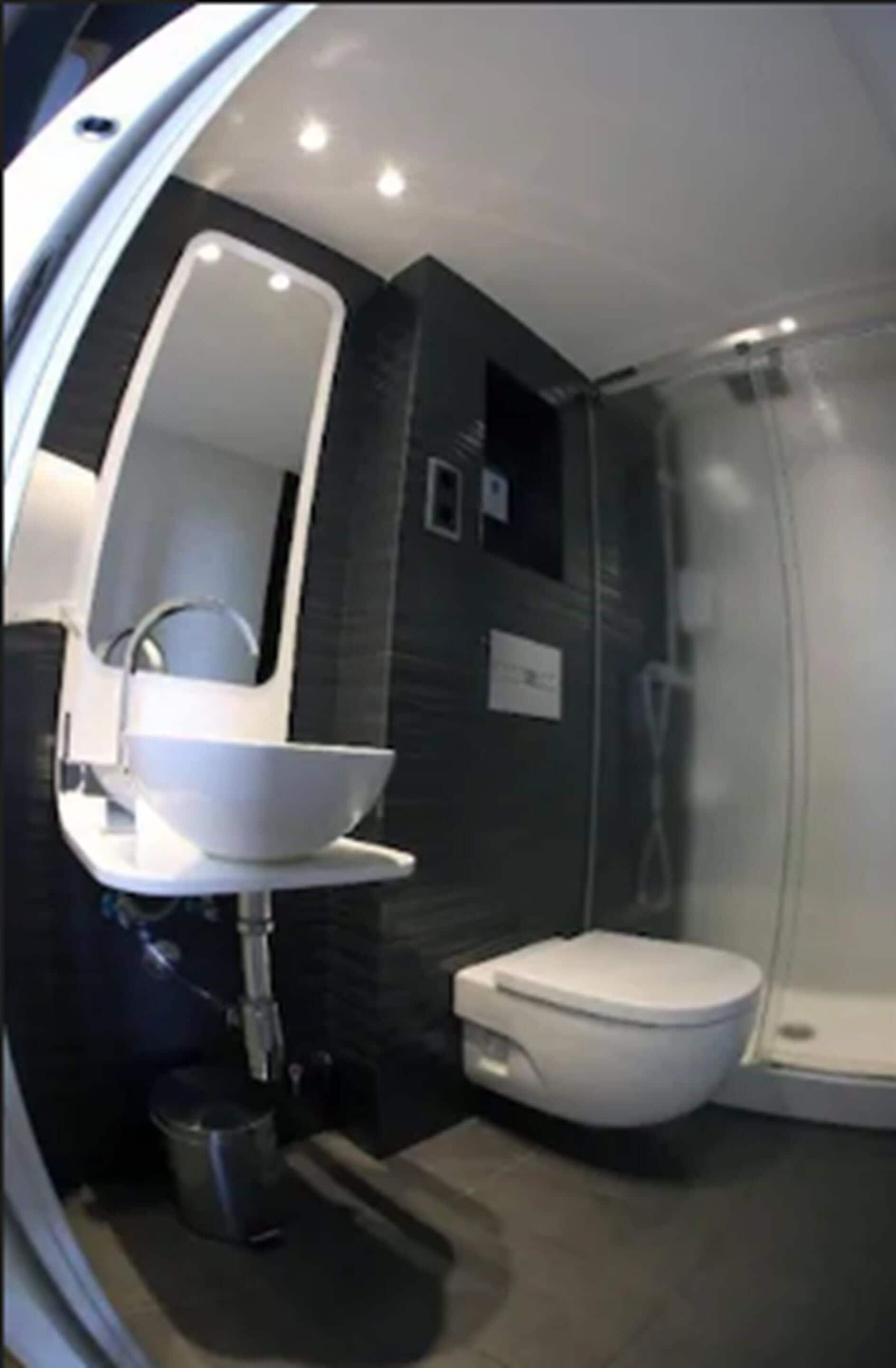 Un baño moderno con lavamanos blanco, espejo, inodoro y cabina de ducha.