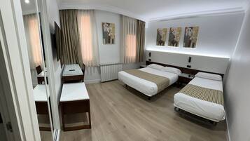 Una habitació d'hotel amb dos llits individuals, un escriptori, una cadira, un televisor i obra d'art a la paret.