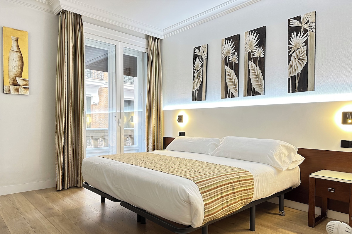 Een hotelkamer met een groot bed, een nachtkastje, een wandlamp en een raam met gordijnen.