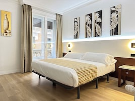 A hotel room with a large bed, a nightstand, a wall-mounted lamp, and a window with curtains.