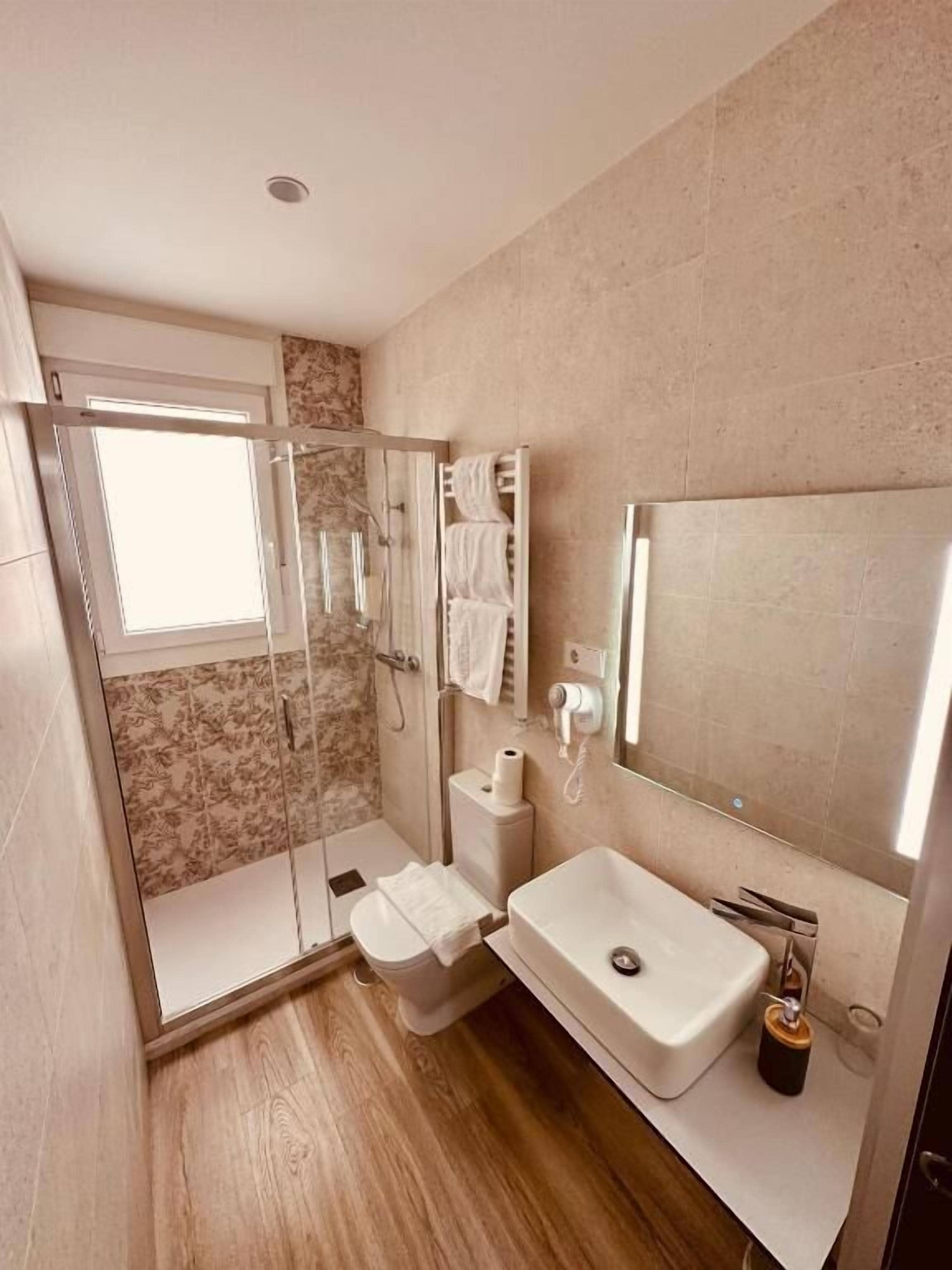 Un baño moderno con ducha envuelta en cristal, inodoro y lavamanos con espejo superior.