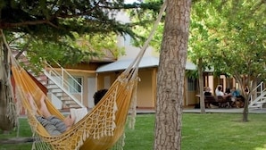 A hammock tied between trees in a grassy area with a building in the background. - El Gualicho Hostel (Puerto Madryn)