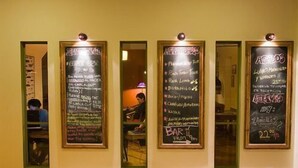 A hallway with four chalkboards displaying menus and prices. - El Gualicho Hostel (Puerto Madryn)