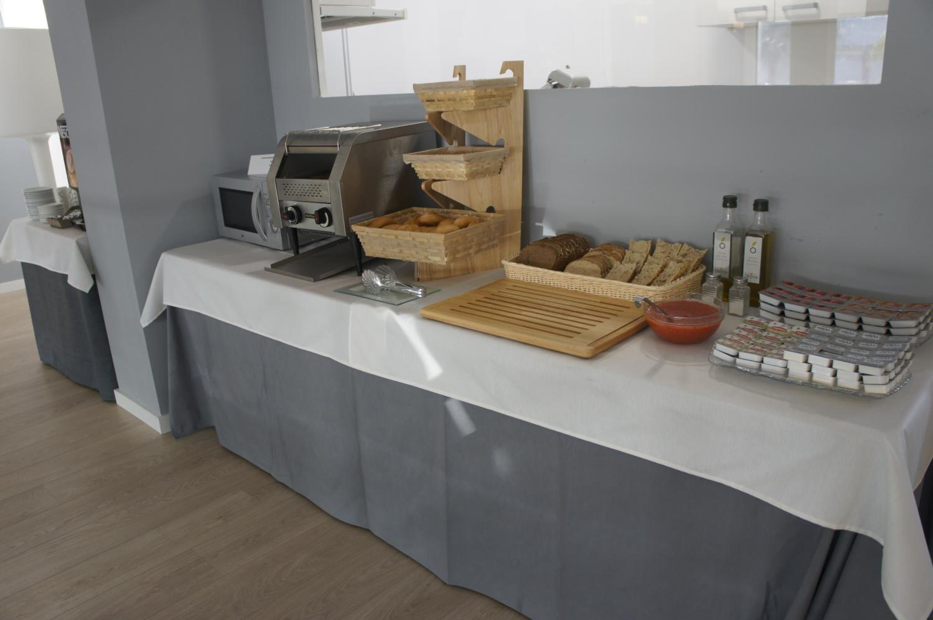 Une table de buffet avec un four à micro-ondes, des paniers à pain, des condiments et des bouteilles d’eau.