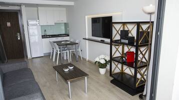Un espacio habitable compacto con kitchenette, una zona de comedor, un televisor montado en la pared y una pequeña estantería.