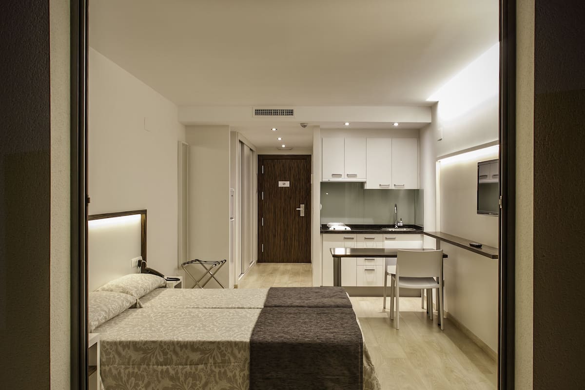 A modern hotel room with a bed, a desk, and a kitchenette.