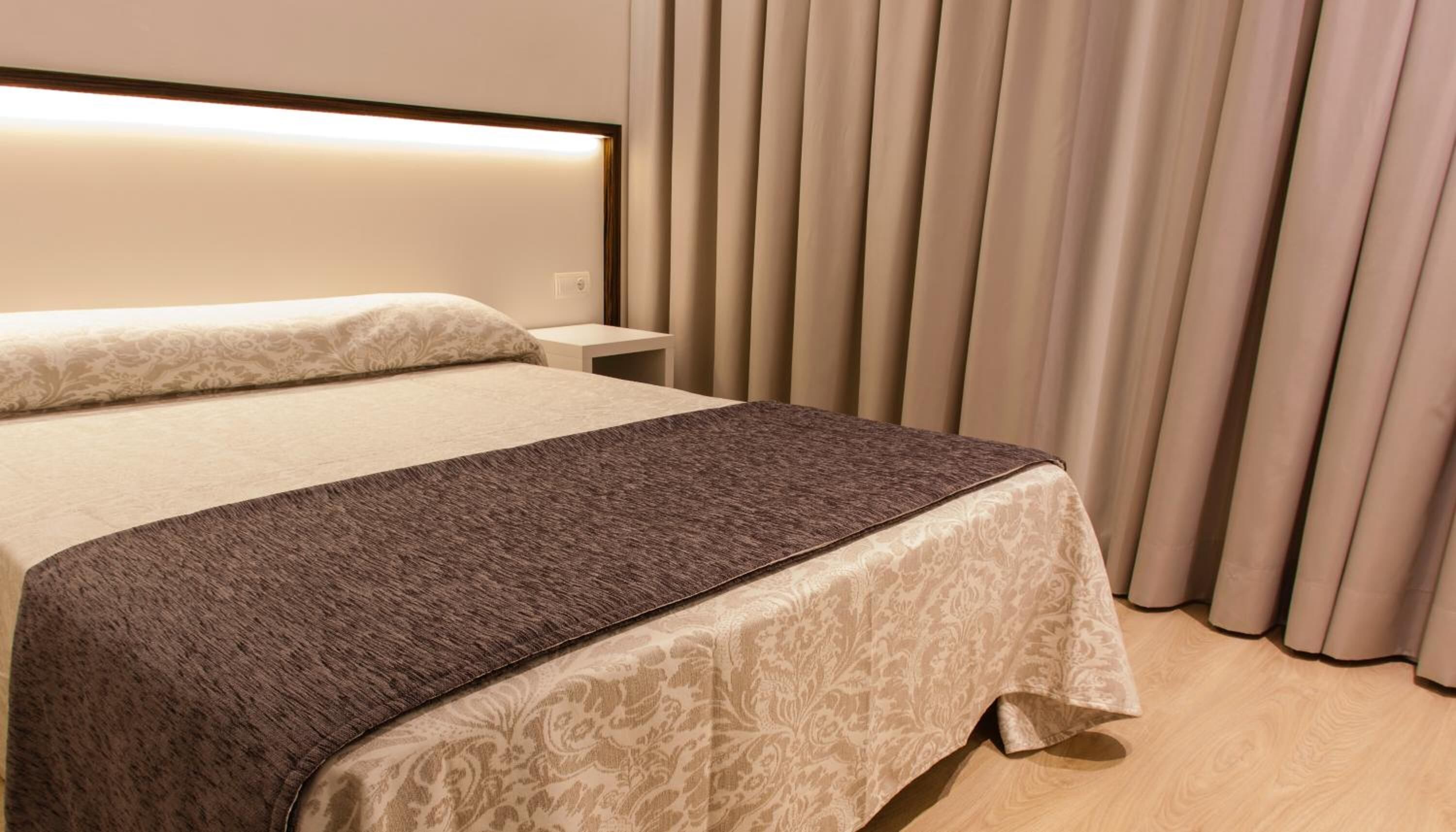 A neatly made bed with a patterned bedspread and a headboard with integrated lighting.