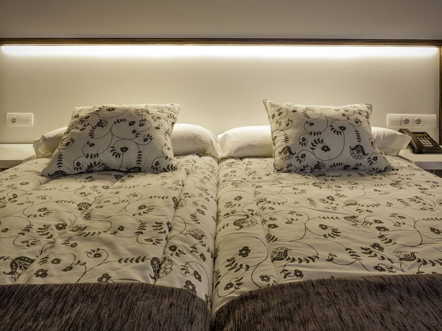 Una cama doble con ropa de cama estampada, dos almohadas, una mesita de noche con un teléfono y una lámpara de pared.