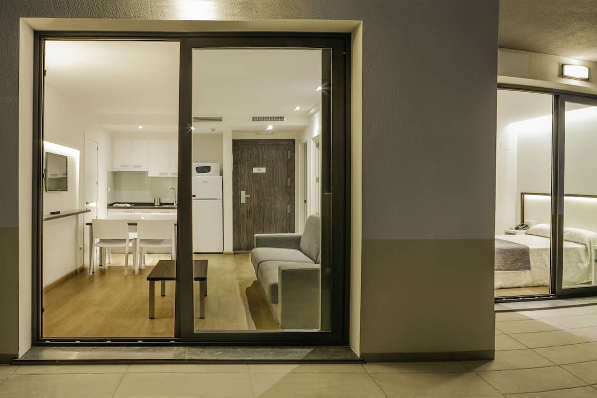 A modern hotel room with a sliding glass door leading to a compact kitchen and living area.