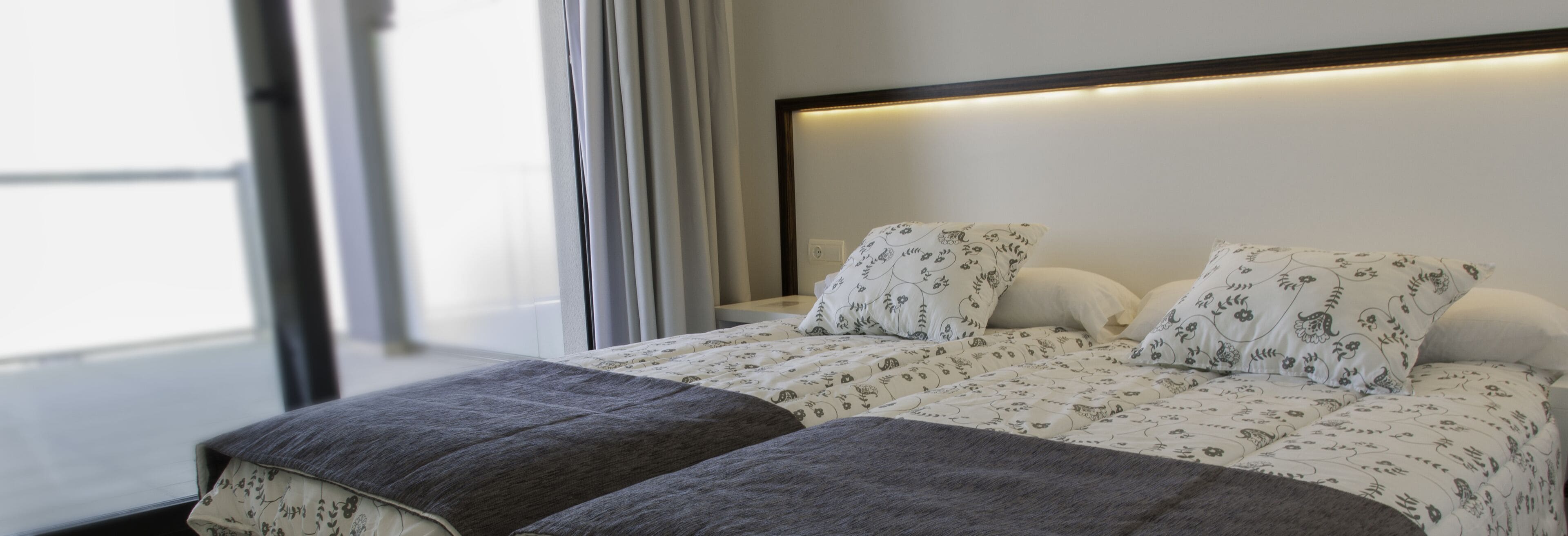 Una cama bien hecha con ropa de cama floral, una mesita de noche y una ventana con cortinas.