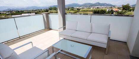 Un balcon avec un canapé blanc, deux chaises blanches et une table basse en verre.
