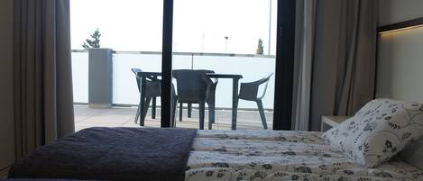 A room with a bed, a small table, and two chairs. There is a balcony with a view of the water.