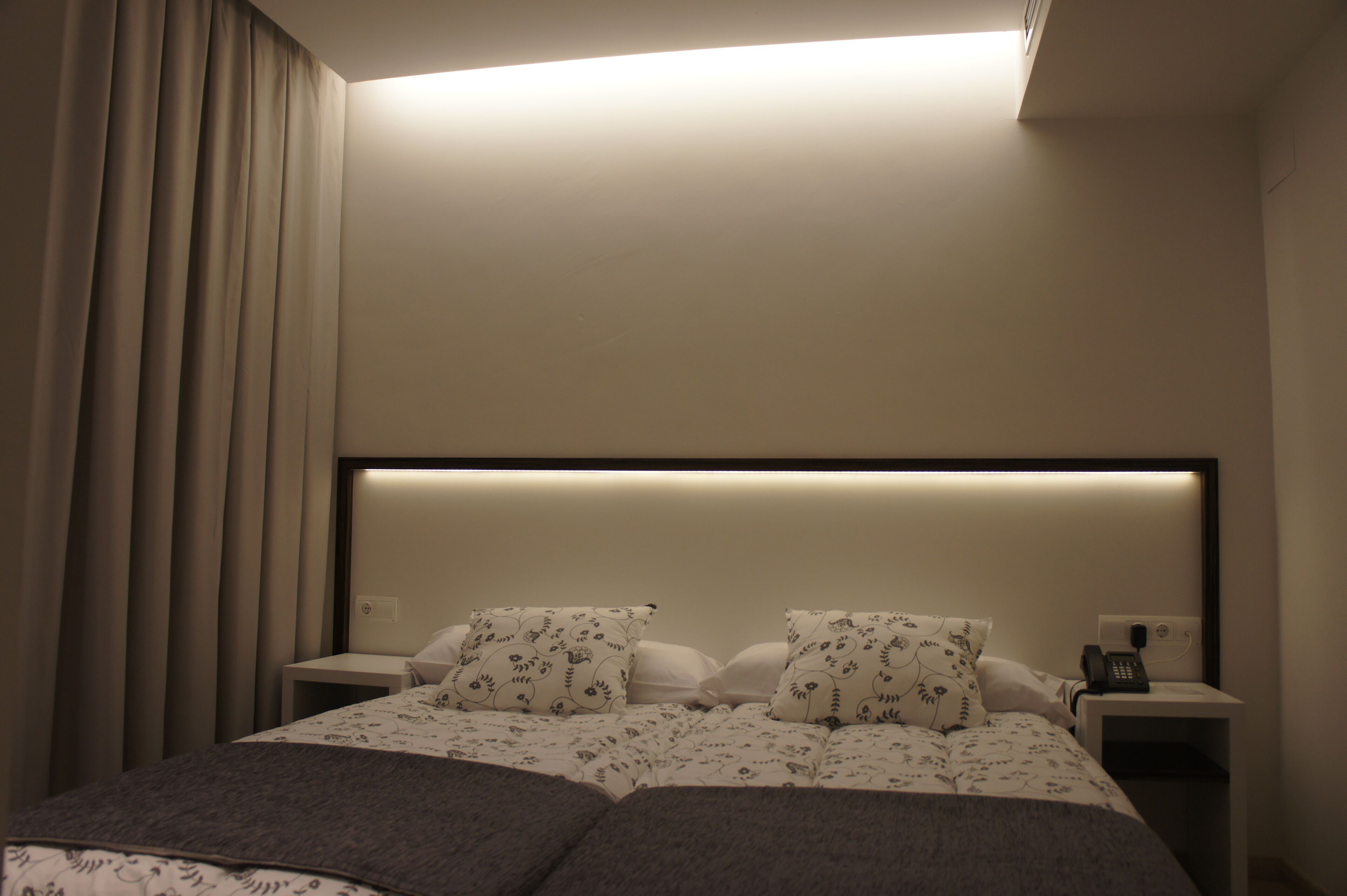 Una habitación de hotel con una cama, dos mesitas de noche, un teléfono y una lámpara en el techo.