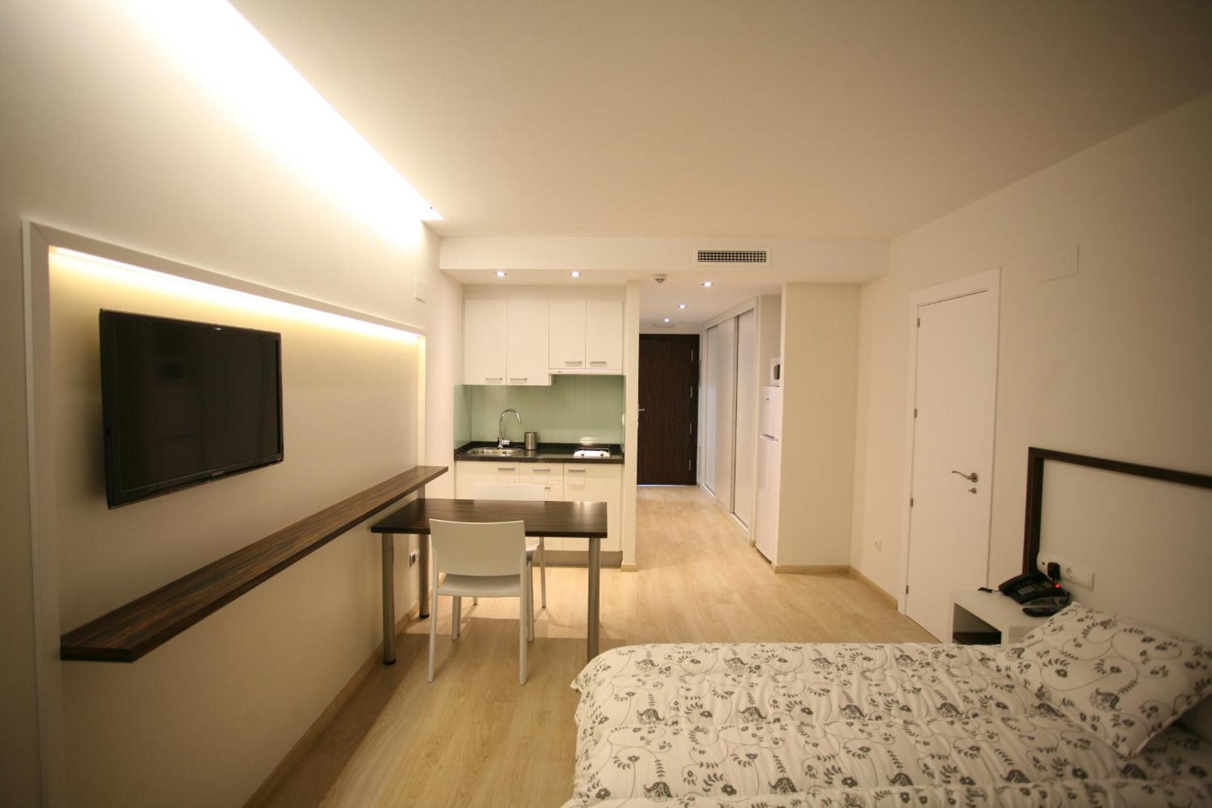 Una camera d'albergo compatta con un letto, un comodino e una TV fissata al muro.