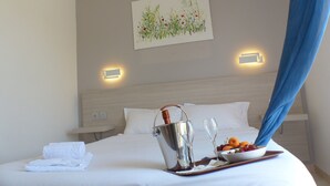 A hotel room with a bed, a painting on the wall, a bucket with a bottle, a tray with fruit and a glass, and a blue curtain. - Stella Marina (Rogliano)