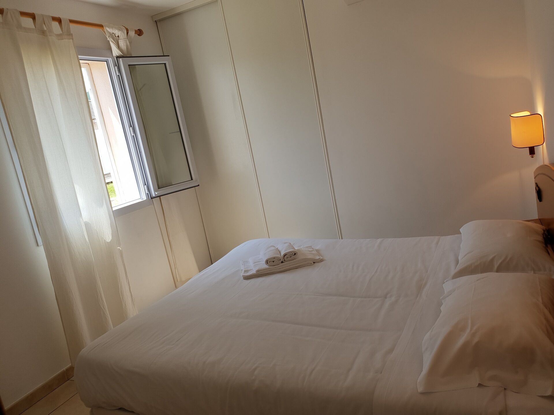 A neatly made bed with a folded towel and a bedside lamp.