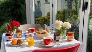 A breakfast table with various food items and drinks, set outdoors with a view of greenery and buildings through a glass door. - Stella Marina (Rogliano)