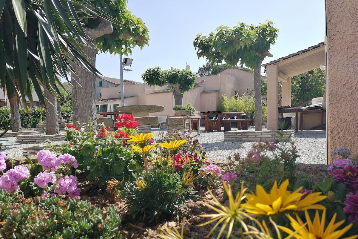 A garden area with various plants and flowers, outdoor seating, and a stone structure.