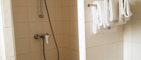 A shower area with a handheld showerhead, a wall-mounted towel rack with multiple towels, and a tiled floor with a brown border.