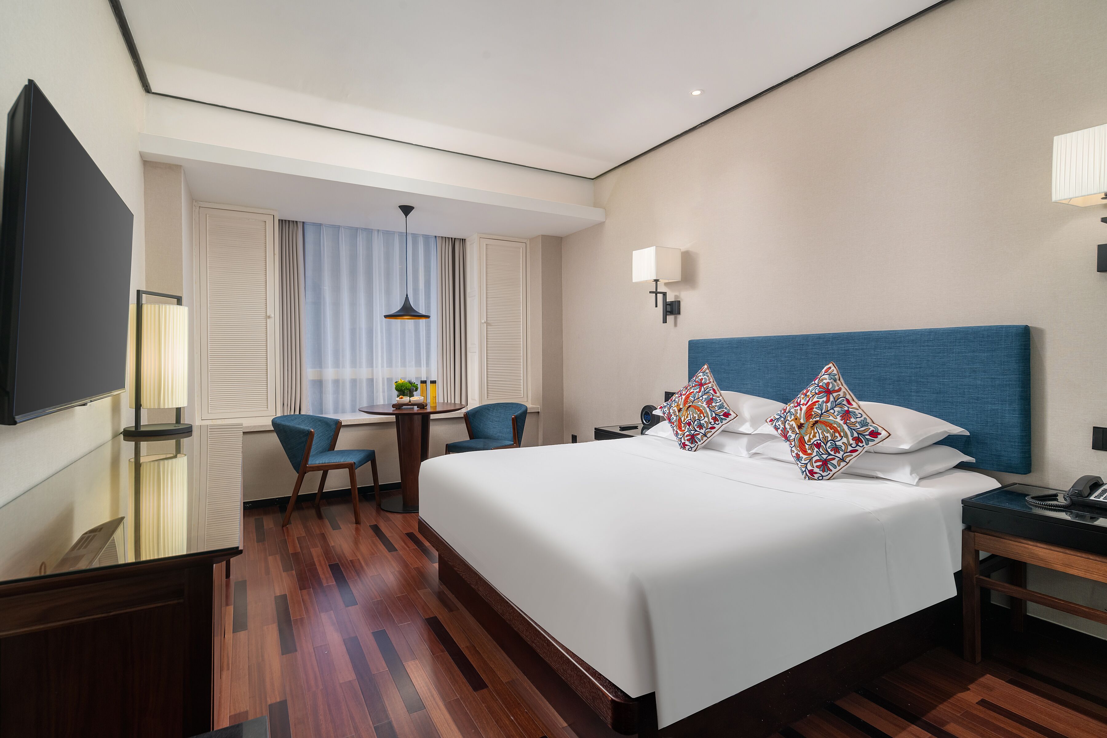 Una habitación de hotel con una cama grande, un escritorio con silla, televisión y ventana con cortinas.