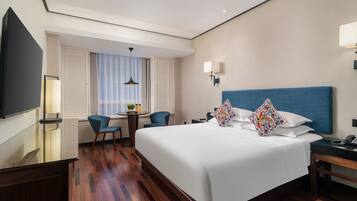 Una habitación de hotel con una cama grande, un escritorio con silla, televisión y ventana con cortinas.
