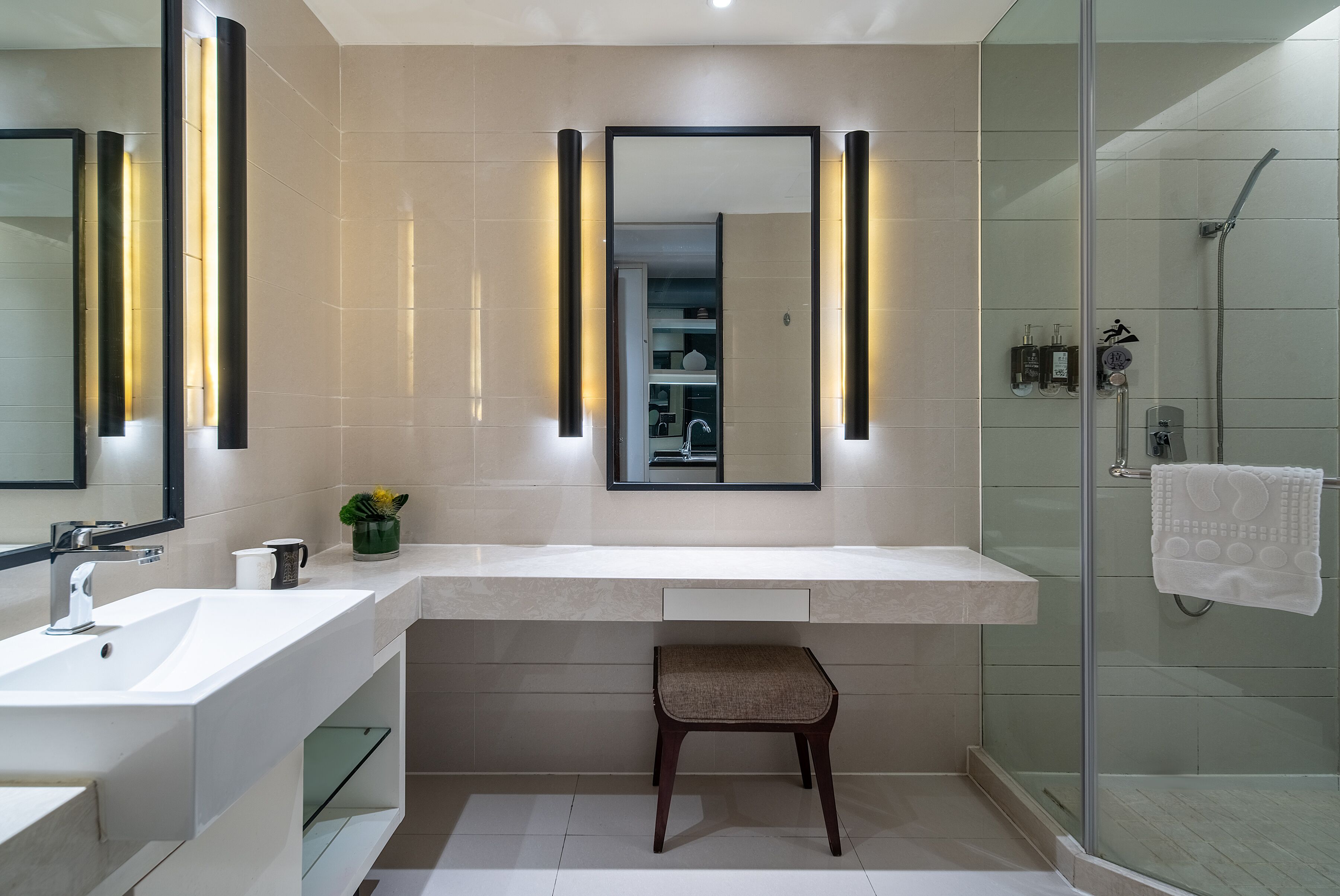 A modern bathroom with a large mirror, a sink, a shower, and a small stool.