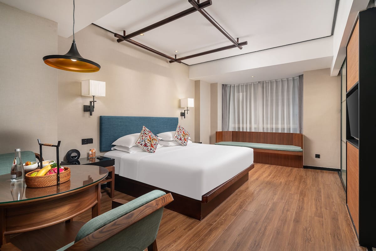 Een hotelkamer met een bed, nachtkastjes, een bureau met stoel, een lamp, een televisie en een raam met gordijnen.