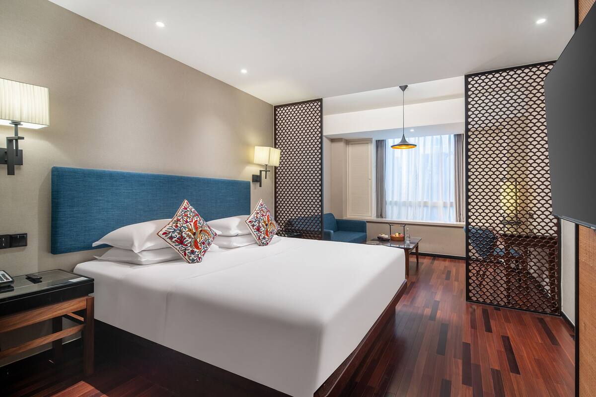 Een hotelkamer met een groot bed, een bureau, een stoel en uitzicht op de stad door het raam.