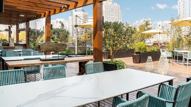 Un espace de restauration en plein air agrémenté de pergolas en bois, de chaises vertes et de tables.